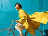 Smiling cyclist in a yellow coat riding past a turquoise wall