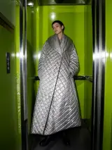 Fashion model in a silver quilted coat standing in a lime-green elevator